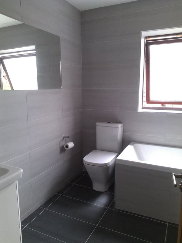 Grey tiled bathroom with a close-coupled toilet and a panelled bath.