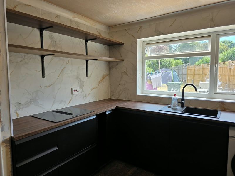Matt black kitchen with walnut-effect worktops, a marble-effect splashback and open shelving.