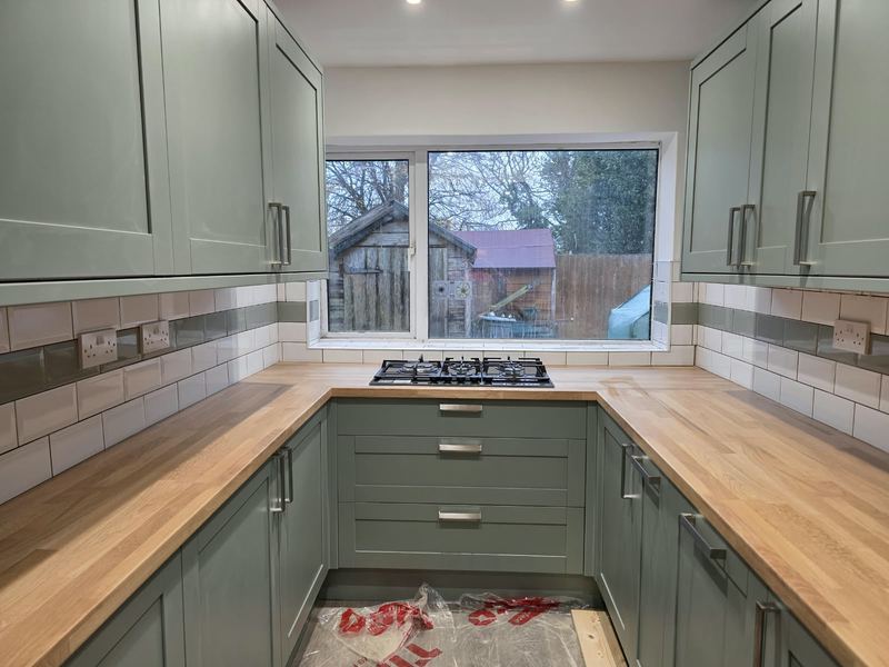 Sage Shaker kitchen with oak worktops in a U-shape under the window