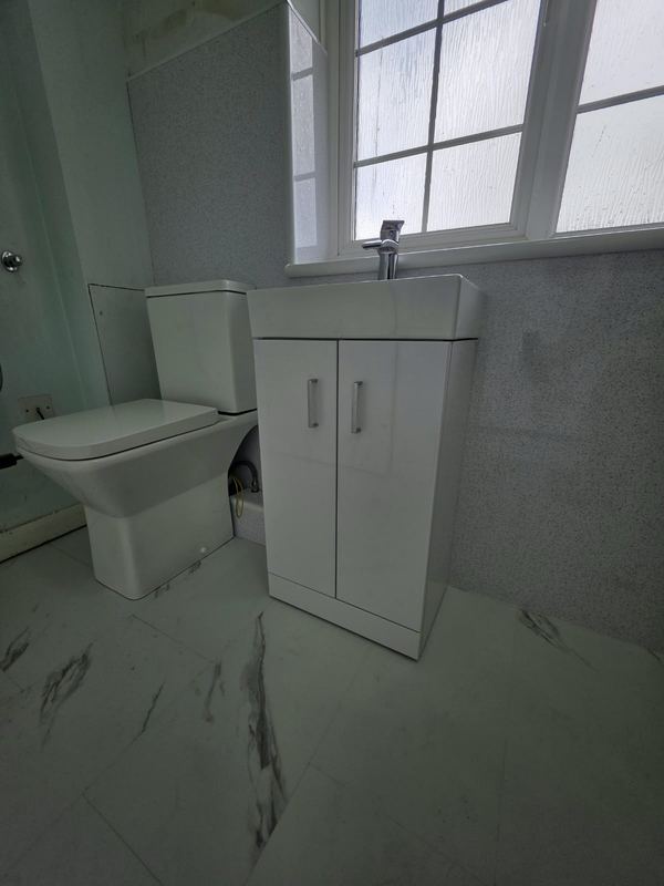 The same shower room: vanity unit, close-coupled toilet and marble-effect floor.