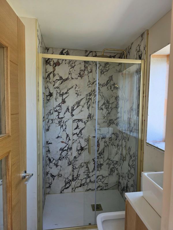 Shower enclosure with marble-effect wall panels and brass-framed sliding doors