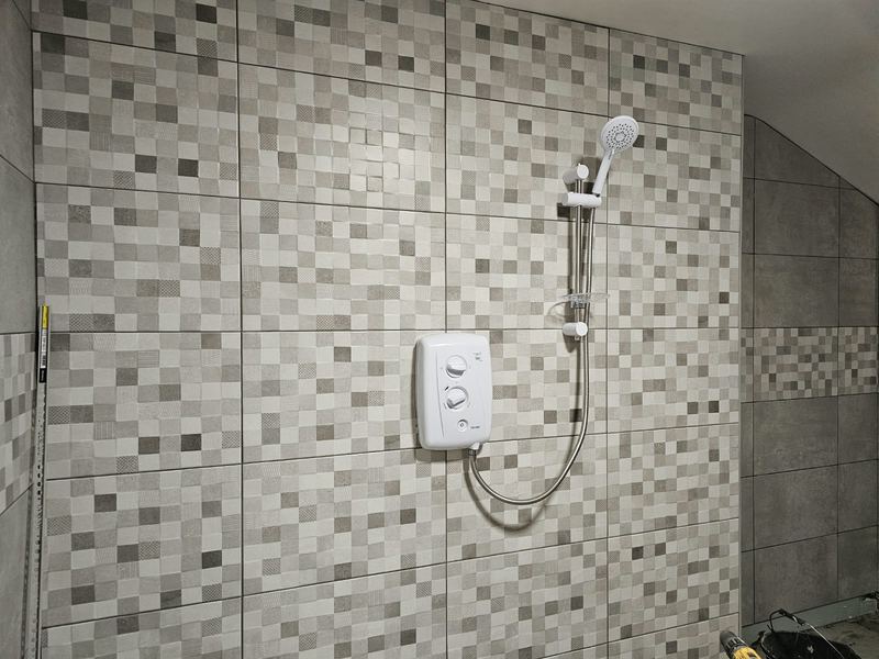 Wetroom shower wall in mosaic-effect tiles, with an electric shower.